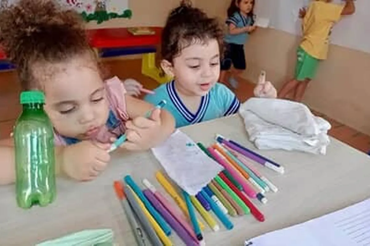 Crianças desenvolvendo atividades de pintura supervisionadas por educadores