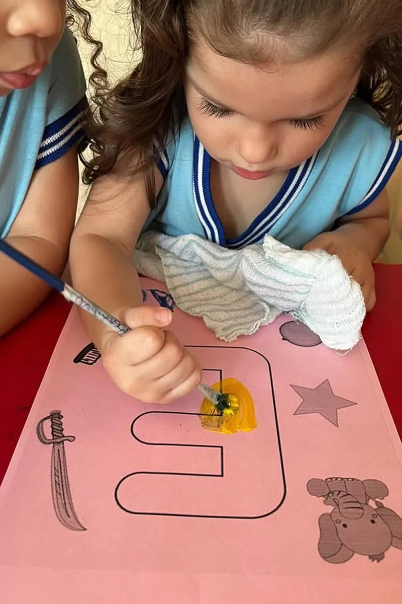 Criança desenvolvendo atividade de escrita com apoio de educadores